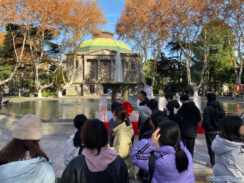 一群年青学生联结在大会堂前的喷池塘广场上，听一位citywalk领队先容东南大学四牌坊校区    影相/佟鑫